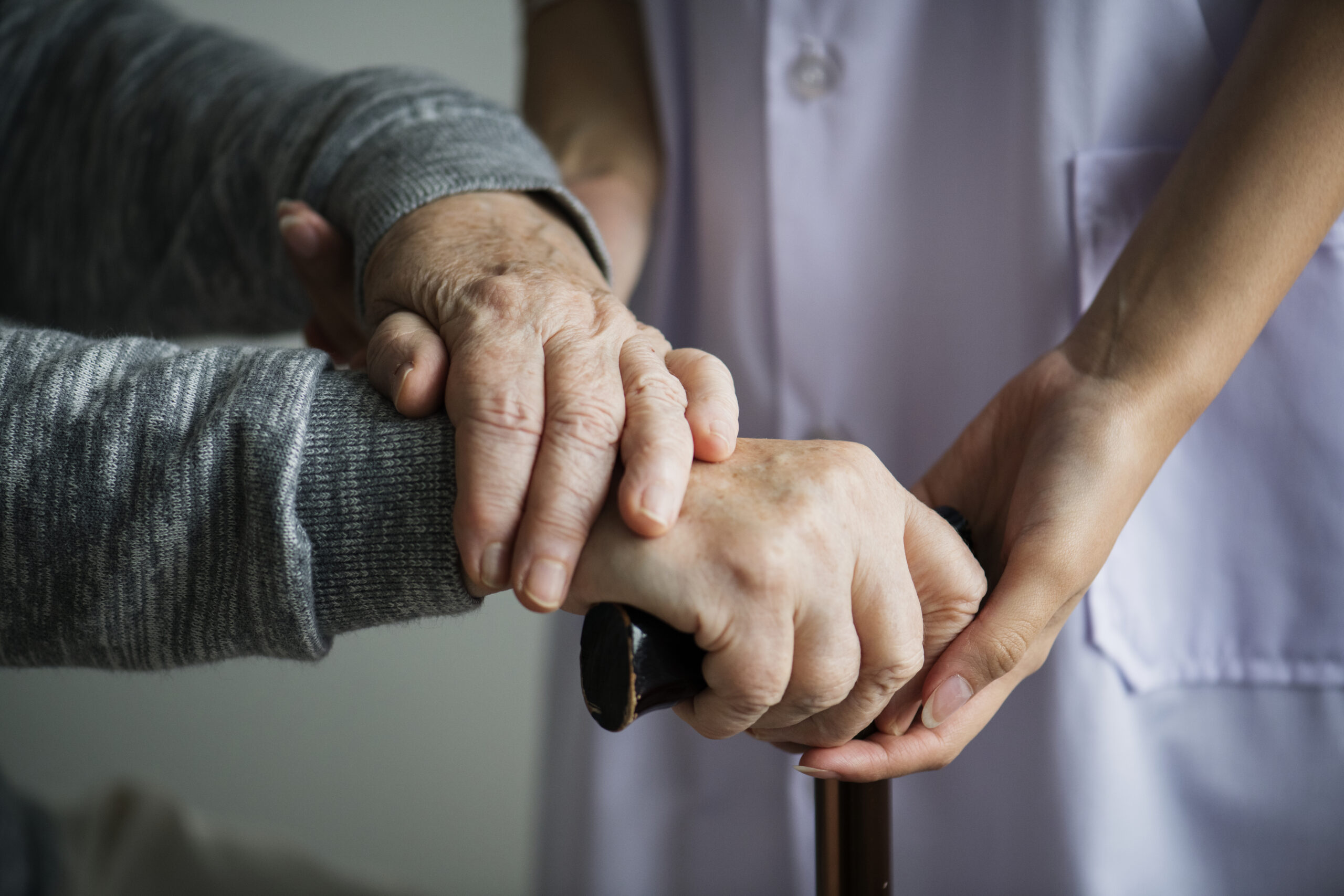 closeup-support-hands elderly hands being offered support by caregiver to grip cane.